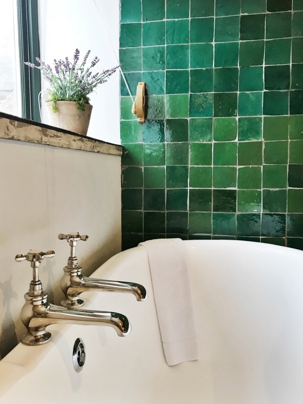 Bath under a window with a green tiled wall